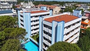 A multi-story hotel with balconies, a swimming pool, and a view of surrounding buildings. - Bright holiday house with a large terrace (Bibione)