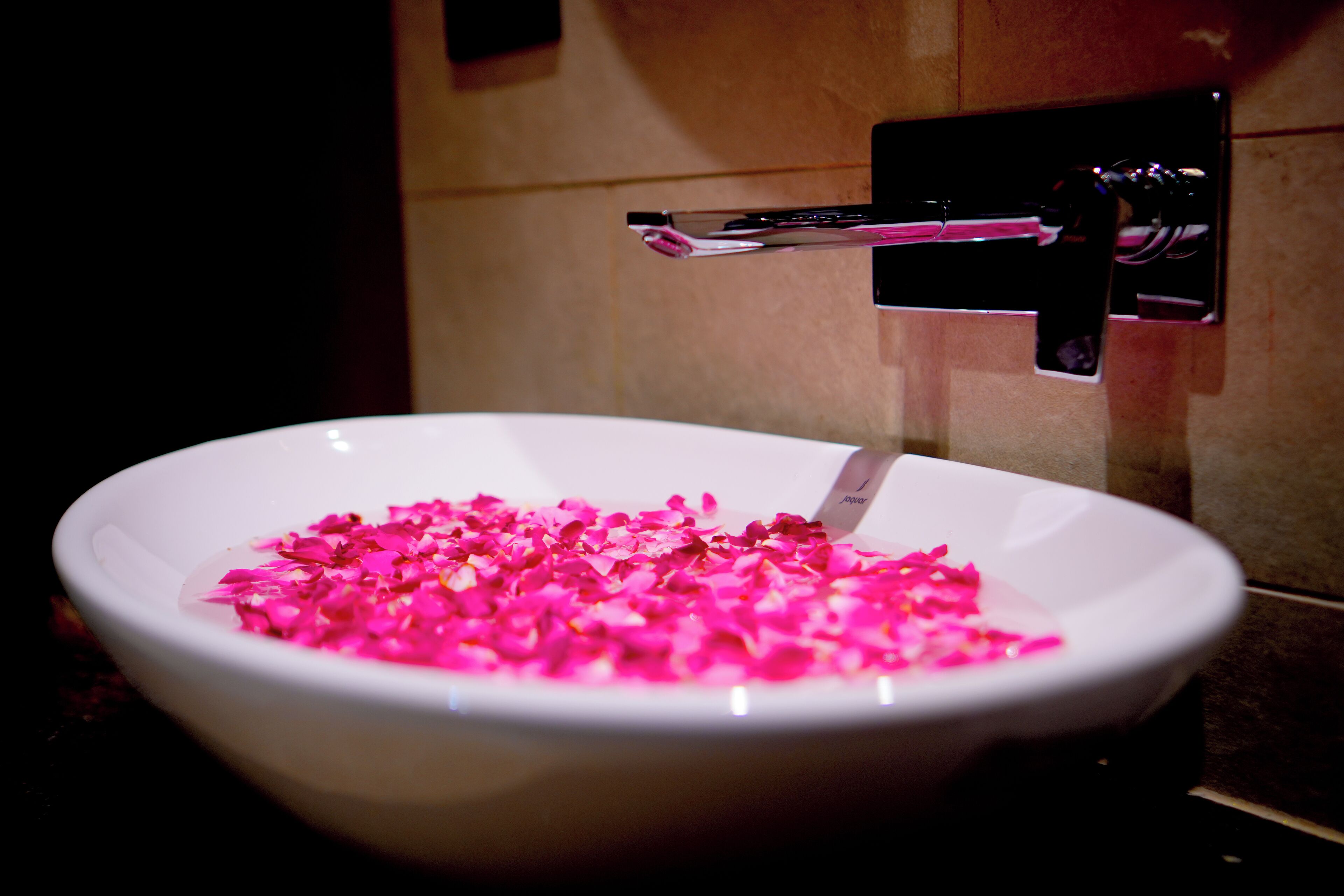 Een witte schaal gevuld met roze bloemblaadjes op een wastafel.