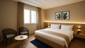Ein Hotelzimmer mit einem großen Bett, zwei Stühlen, einem kleinen Tisch und einem Fenster mit Vorhängen.