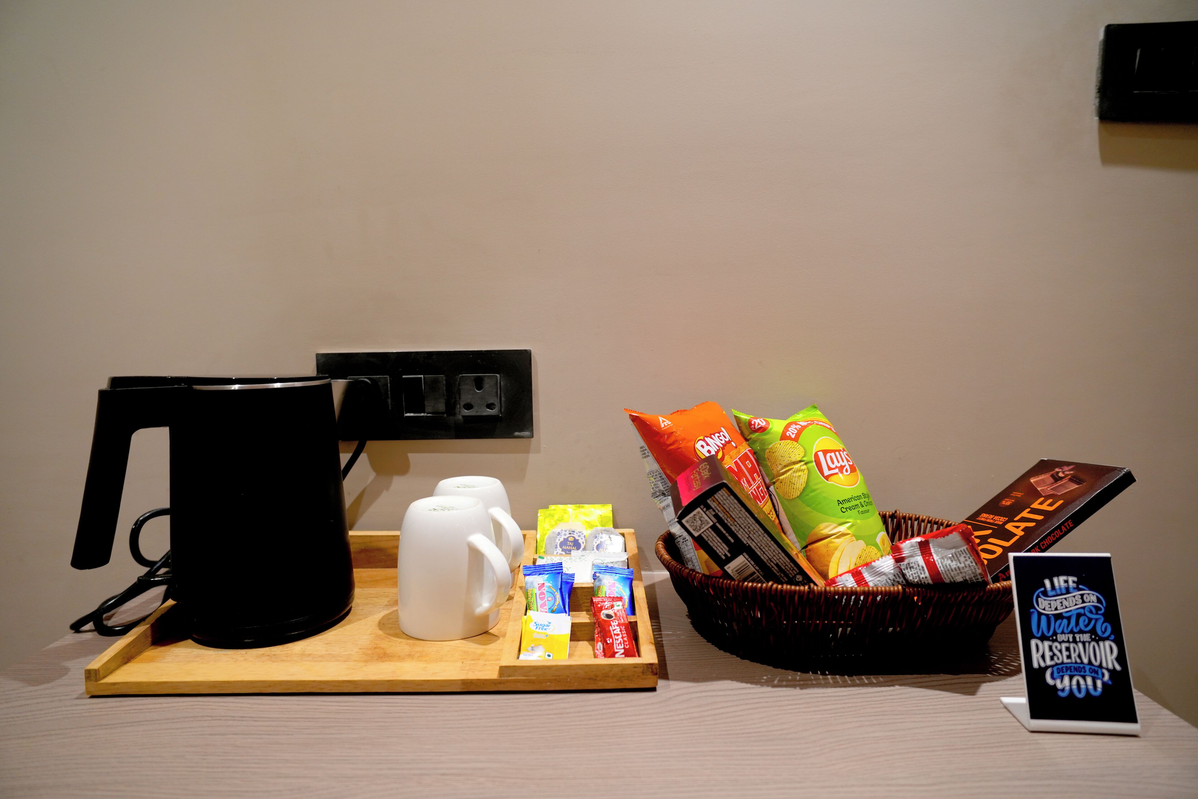 A coffee station with a coffee maker, mugs, snacks, and a sign about water conservation.