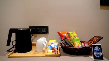 A coffee station with a coffee maker, mugs, snacks, and a sign about water conservation.