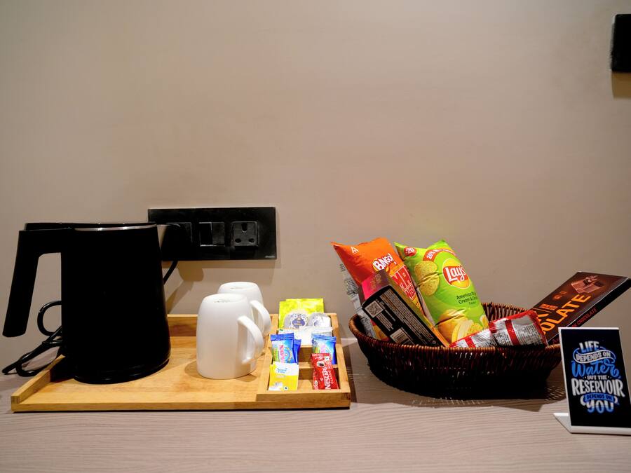 A coffee station with a coffee maker, mugs, snacks, and a sign about water conservation.