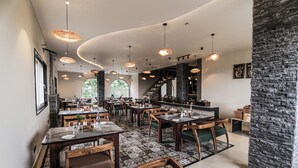 Ein Restaurant mit mehreren Tischen und Stühlen, einer Steinwand und hängenden Pendelleuchten.