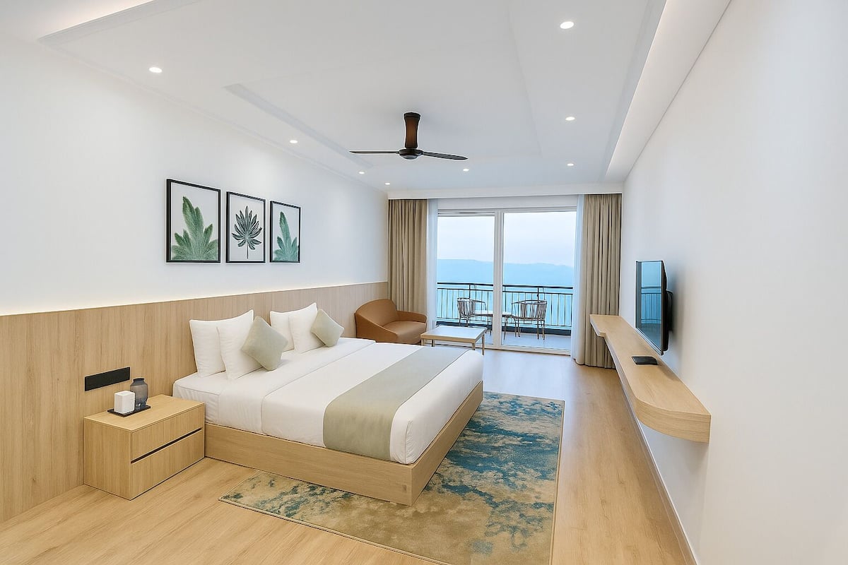 A modern hotel room with a large bed, a desk, a chair, a TV, and a balcony with a view.