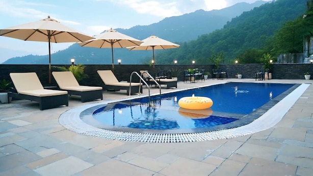 Ein Swimmingpool mit Liegestühlen und Sonnenschirmen, umgeben von einer Steindeck und einer Bergkulisse.