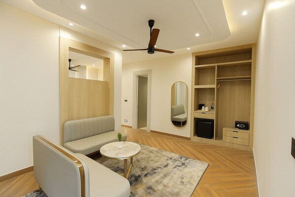 A modern hotel room with a sofa, a round coffee table, a mirror, a wardrobe, and a ceiling fan.