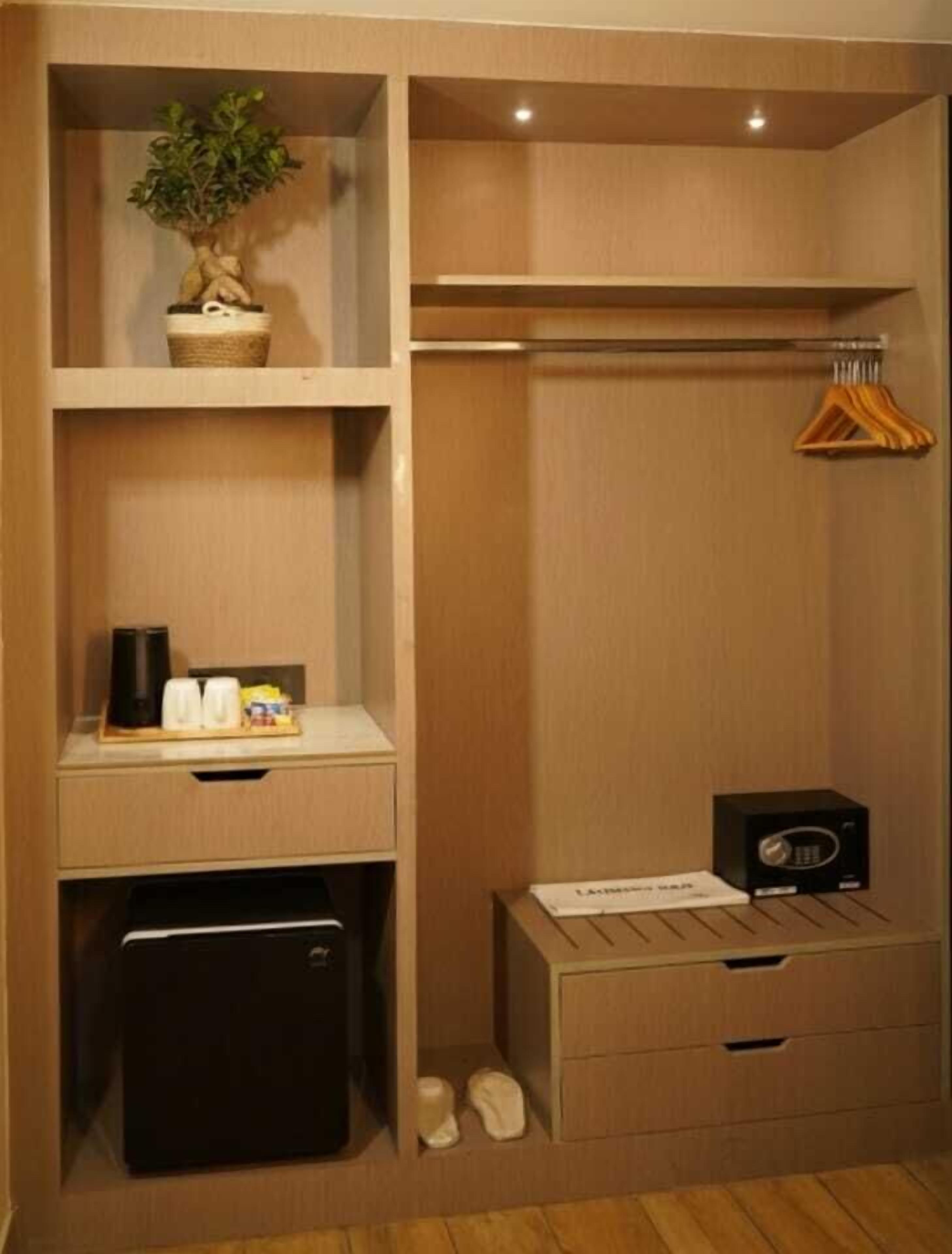 A compact hotel room with a built-in wardrobe, a small desk with a coffee maker, a radio, and a shoe rack.