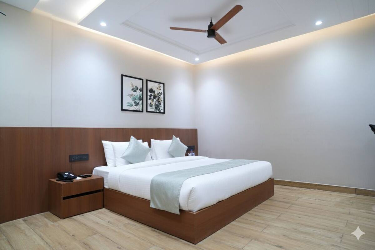 A modern hotel room with a large bed, wooden headboard, a nightstand, and a ceiling fan.