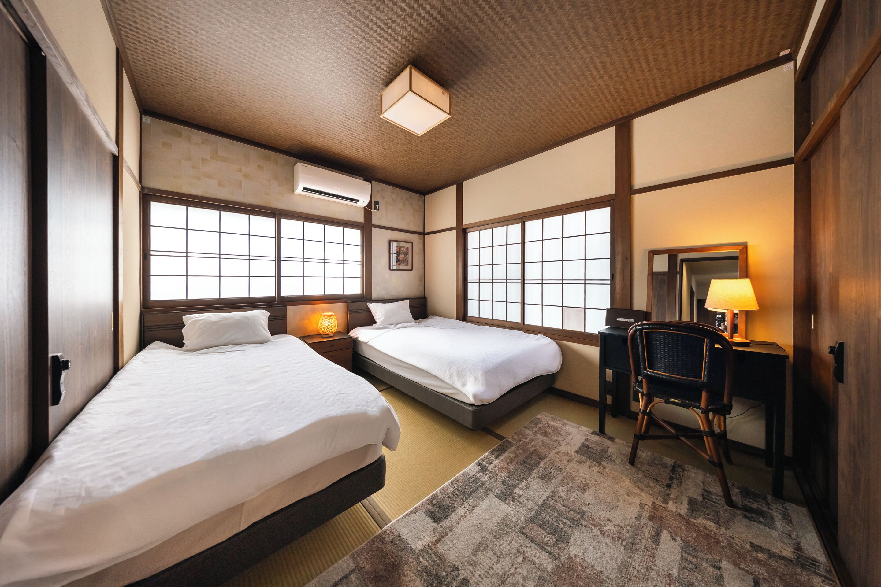A hotel room with two beds, a desk, a chair, and a large window.