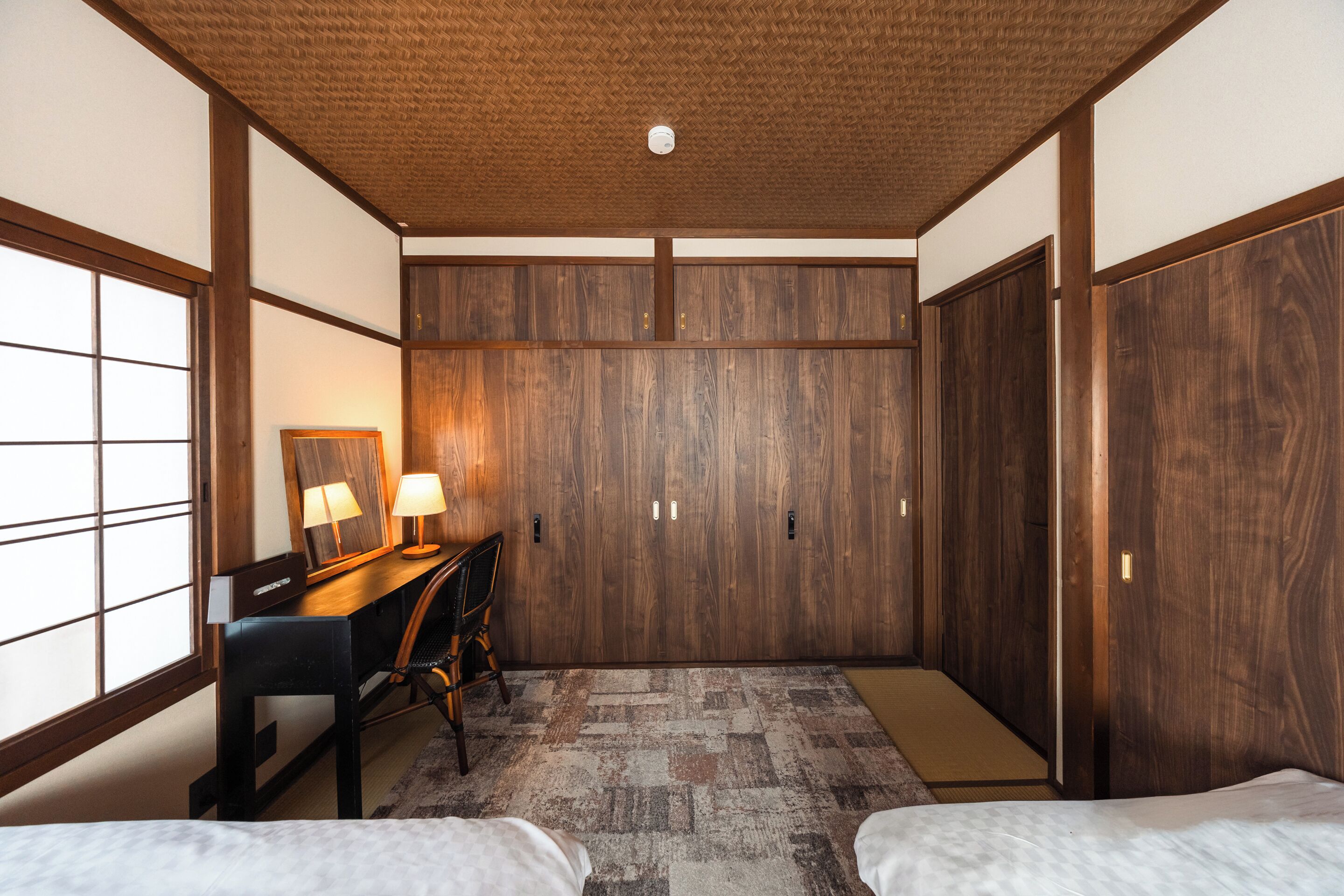 Habitación de hotel con decoración tradicional japonesa, que incluye suelo de tatami, un escritorio con lámpara y un armario.
