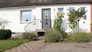 Una casa residencial con puerta gris, un pequeño jardín delantero y un camino de entrada pavimentado.