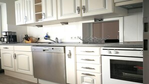 Una cocina con armarios blancos, lavavajillas, estufa y cafetera.