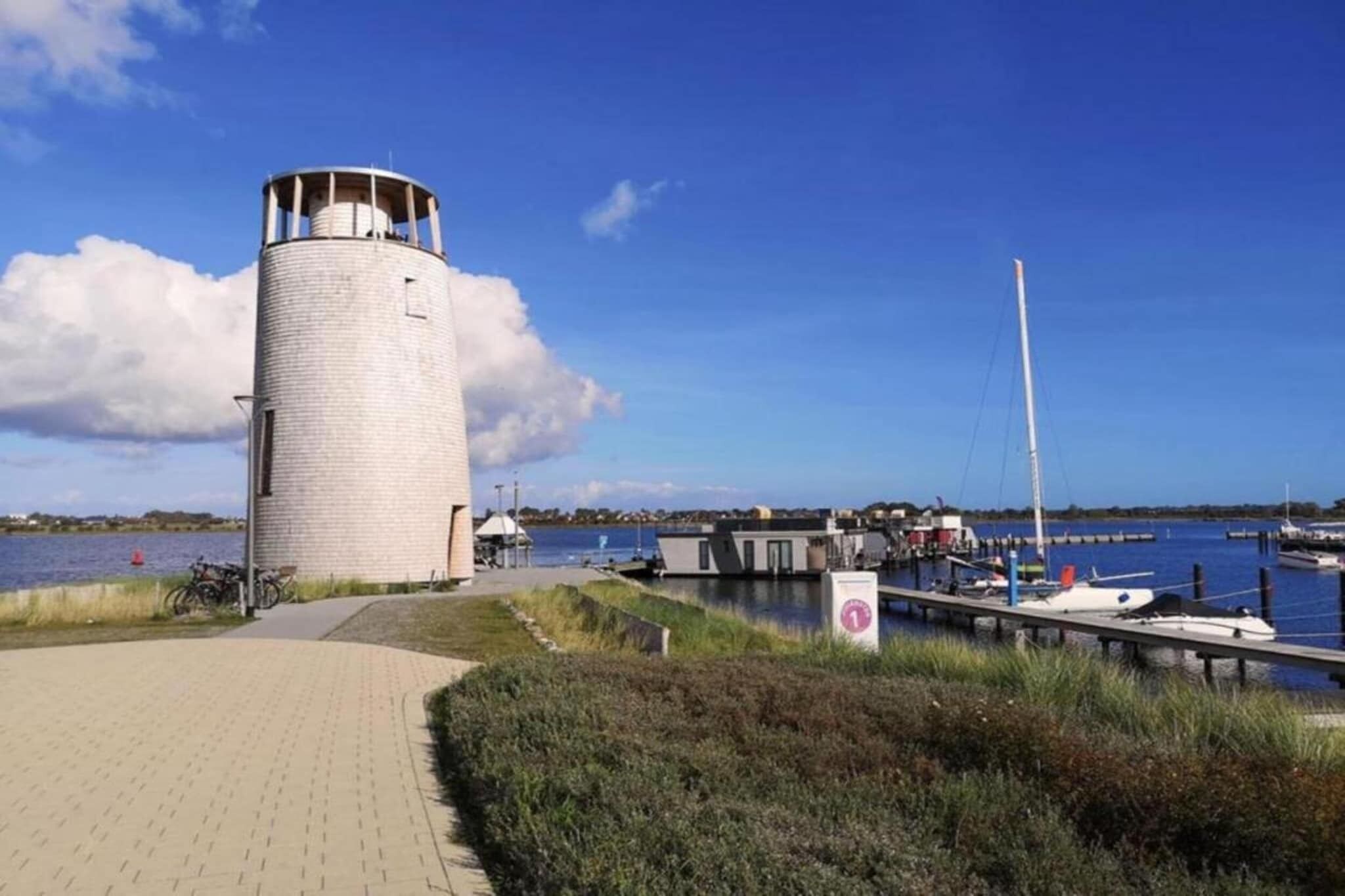 A lighthouse by a marina with a paved walkway and boats.