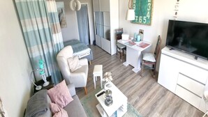 A modern living room with a sofa, a coffee table, a TV, a desk, and a wardrobe. - Coastal Apartment with Balcony (Fehmarn OT Burgtiefe-Südstrand)