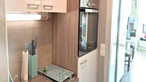 A compact kitchen with a built-in oven, a small countertop, and a paper towel holder. - Coastal Apartment with Balcony (Fehmarn OT Burgtiefe-Südstrand)
