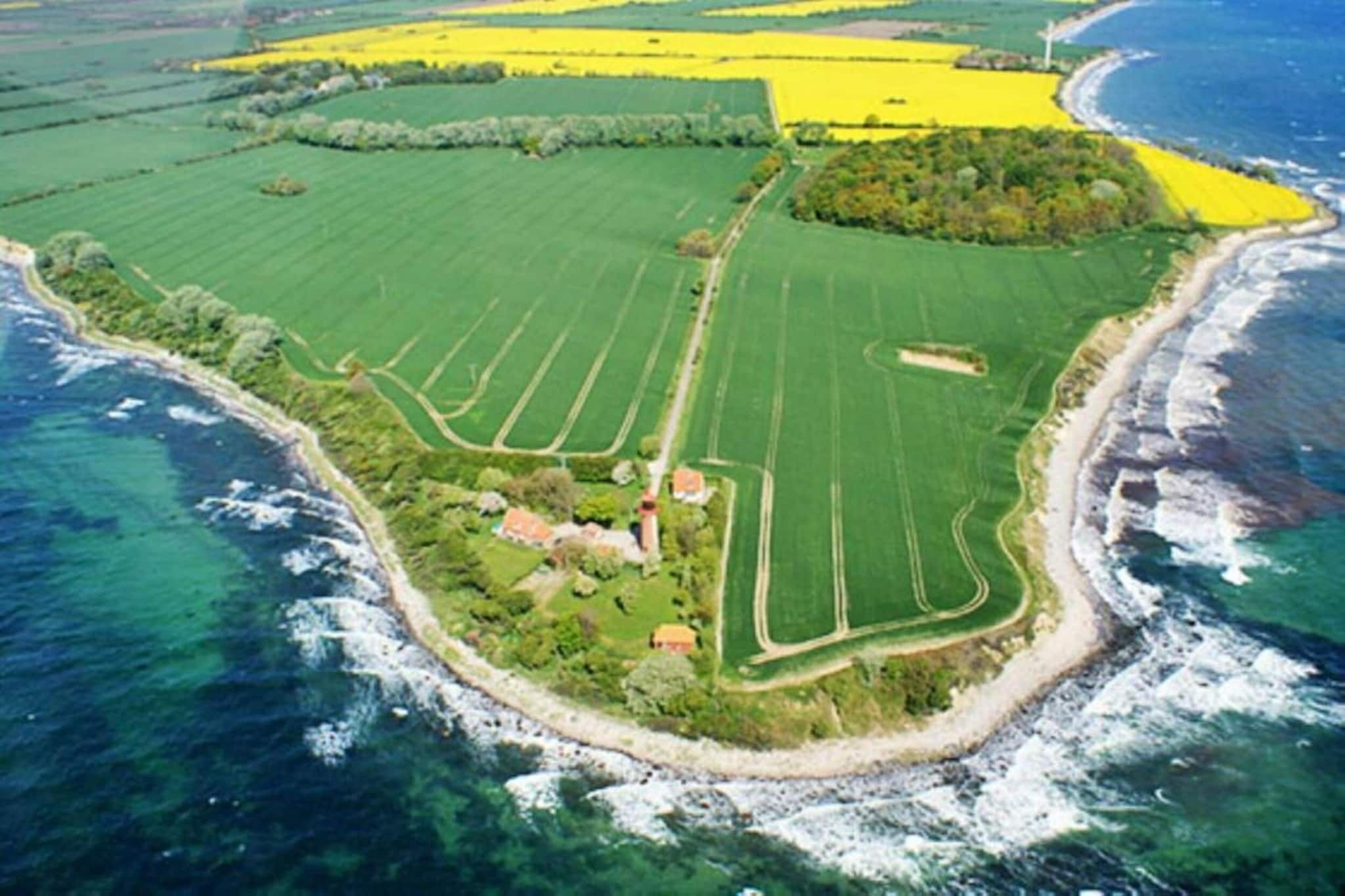 Luftaufnahme eines Küsteneigentums mit grünen Feldern, einem Strand und einem Leuchtturm.