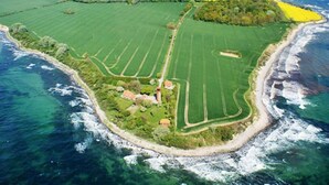 An aerial view of a coastal property with green fields, a beach, and a lighthouse. - Coastal Apartment with Balcony (Fehmarn OT Burgtiefe-Südstrand)