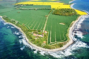 Luchtbeeld van een kustbezit met groene velden, een strand en een vuurtoren.