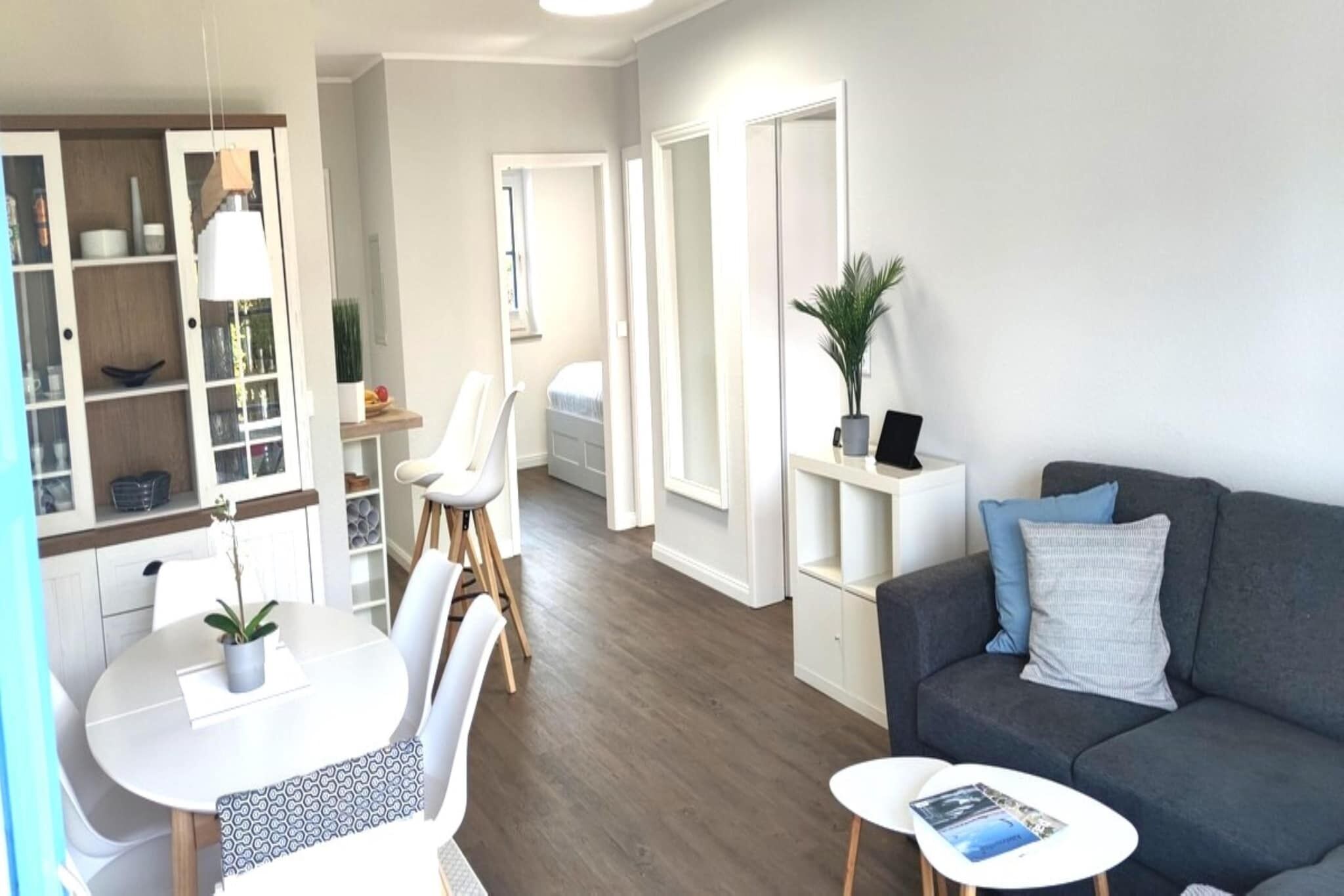 Una sala de estar moderna con un sofá gris, una mesita blanca y un comedor con una mesa y sillas blancas.