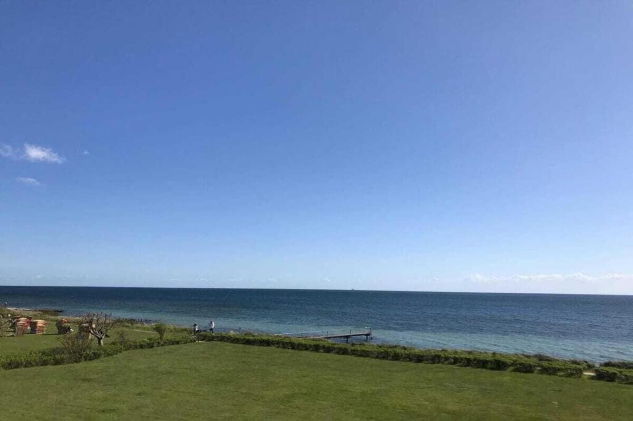 Uitzicht op de kust met een grasveld, een pier en de zee.