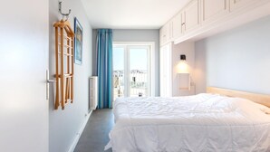 A bedroom with a bed, a window with curtains, a radiator, and a wall-mounted coat rack. - Apartment met zeezicht in Oostende (OOSTENDE)
