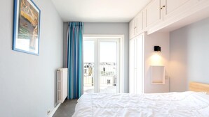 Ein Schlafzimmer mit einem großen Bett, einem Heizkörper, einem Fenster mit Vorhängen und Blick auf Gebäude.