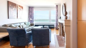 A modern living room with a sofa, two armchairs, a coffee table, and a view of the sea through large windows. - Apartment met zeezicht in Oostende (OOSTENDE)