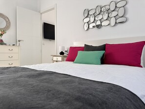 A modern bedroom with a bed, a dresser, a mirror wall art, and a television on the wall.