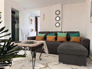 A living room with a grey sectional sofa, a marble floor, and a table with a vase and remote control.