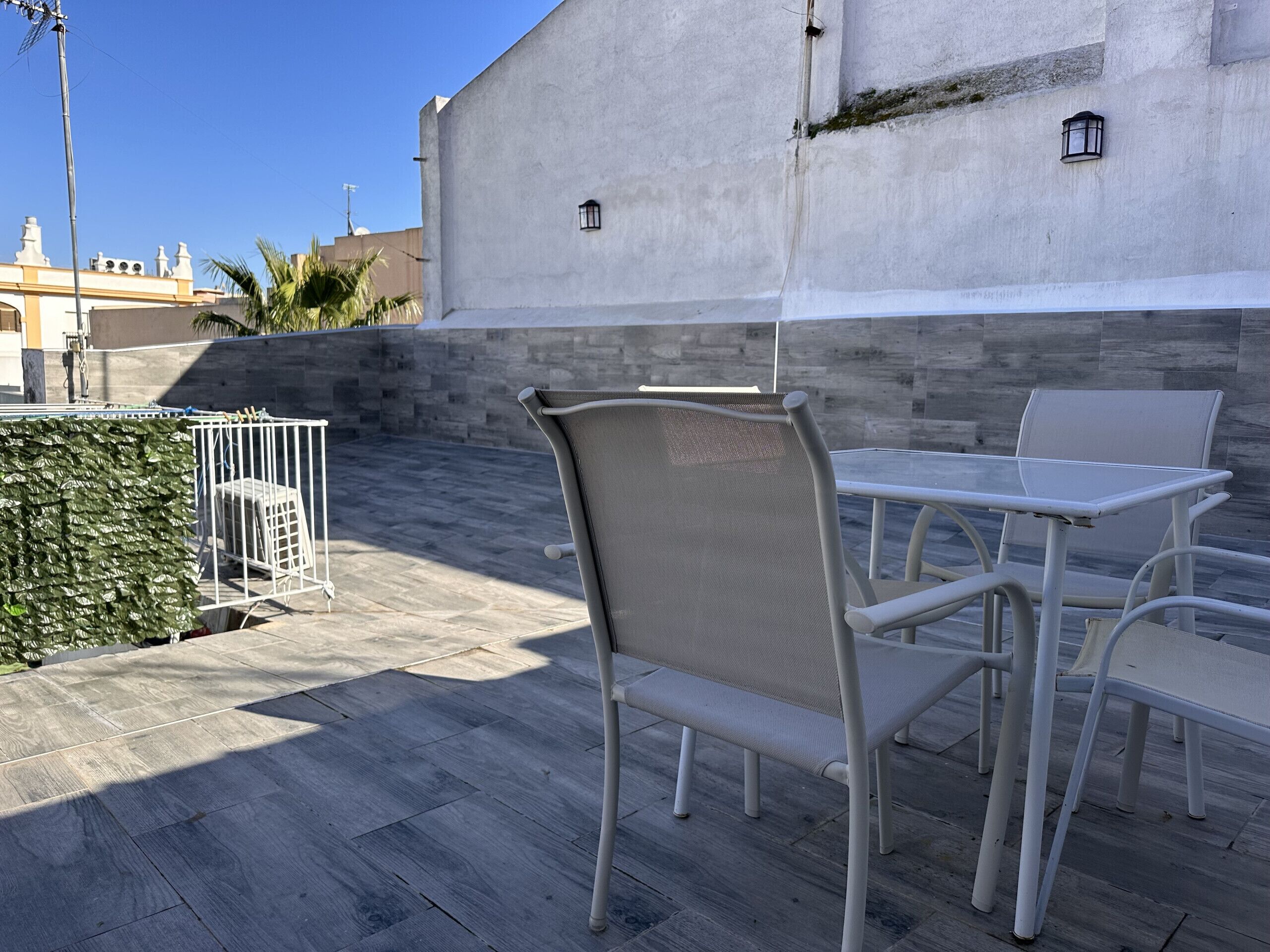 Un patio al aire libre con sillas y mesas de metal blanco, un muro de piedra y una valla metálica.