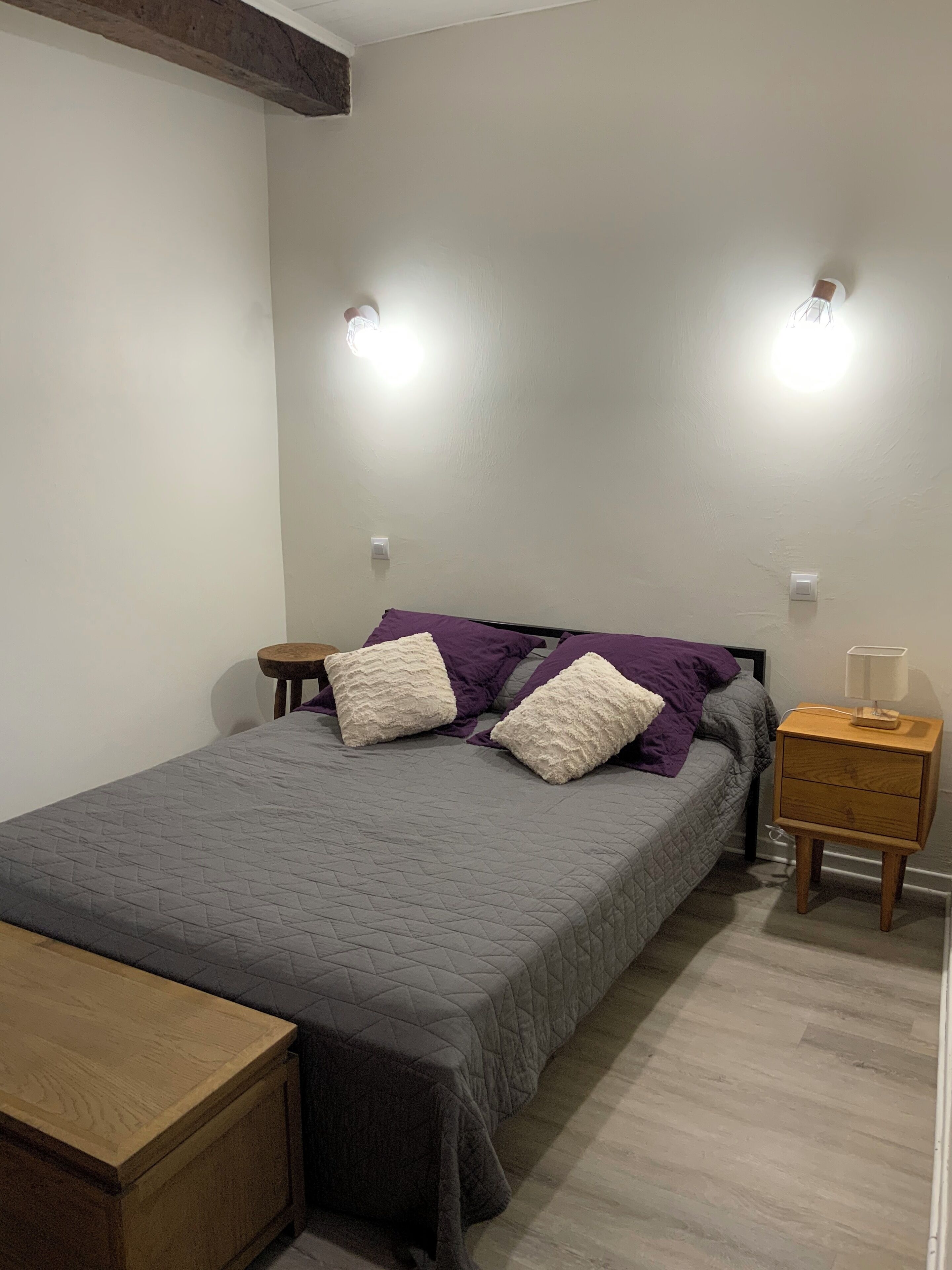 Een slaapkamer met een bed, twee nachtkastjes, een bijzettafeltje en een houten bankje.