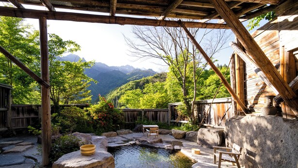 A traditional wooden structure with a stone pond, wooden benches, and a view of mountains. - Ryokan Yakenoyu (Takayama)