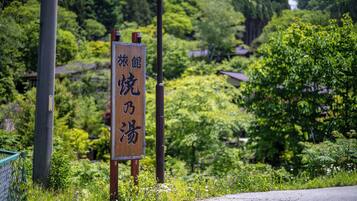 A wooden sign with Japanese characters, surrounded by lush greenery and a road.