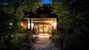 A traditional Japanese building with a wooden entrance, surrounded by lush greenery and a stone pathway leading to the door. - Ryokan Yakenoyu (Takayama)