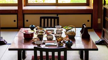 Ett traditionellt japanskt matbord med olika rätter och serveringsredskap, placerat i ett rum med tatamimattor på golvet och utsikt över grönskan genom stora fönster.