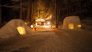A snow-covered path leading to a lit building with a snow igloo on either side. - Ryokan Yakenoyu (Takayama)