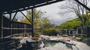 A rustic wooden structure with a stone pond, wooden benches, and a table. - Ryokan Yakenoyu (Takayama)