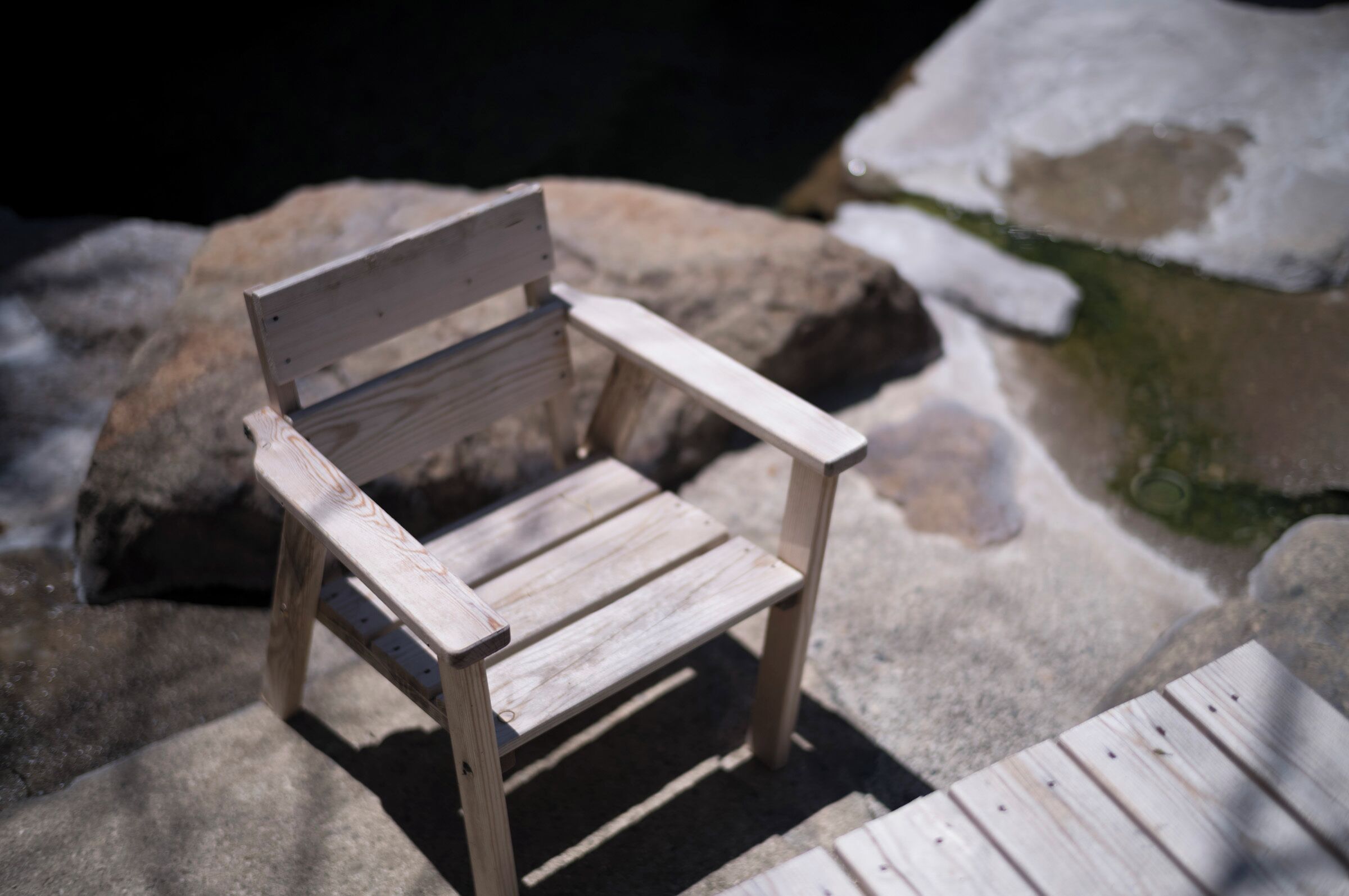 Un banc en bois, doté d’un dossier et d’accoudoirs, est placé sur une surface en pierre, avec quelques plaques de neige à proximité.