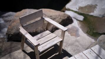 Un banc en bois, doté d’un dossier et d’accoudoirs, est placé sur une surface en pierre, avec quelques plaques de neige à proximité.