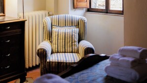 A room with a striped armchair, a lamp, a window with wooden shutters, and a radiator. - Sanniccolo'20 - Historic Residence (Arezzo)