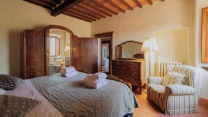 A bedroom with a bed, a wooden wardrobe, a chair, and a lamp. - Sanniccolo'20 - Historic Residence (Arezzo)