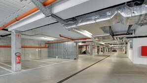 Un estacionamiento subterráneo moderno y limpio, con pisos de concreto, barandales de metal y extintores visibles.