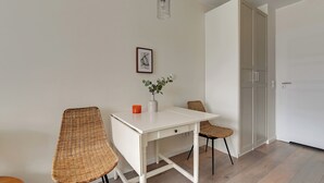 Un comedor con una mesa blanca, sillas de mimbre, un jarrón con una planta y un cuadro en la pared.