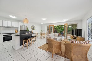A modern kitchen with white cabinets, a central island with stools, and a dining area with a round table and chairs. - Brunswick Beach Club - Coastal Comfort Near Beach, Pet Friendly (COFFS HARBOUR)