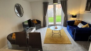 A modern living room with a sofa, a dining table, and a TV. - Radbourne House - Spacious 2 Bed, Home from Home (Derby)