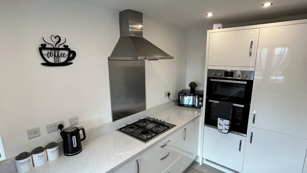 A modern kitchen with white cabinets, a stainless steel range hood, a built-in oven, and a coffee maker on the counter. - Radbourne House - Spacious 2 Bed, Home from Home (Derby)