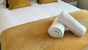 A neatly made bed with a white comforter, two black and two mustard-colored pillows, a rolled white towel, and a woven throw blanket. - Radbourne House - Spacious 2 Bed, Home from Home (Derby)