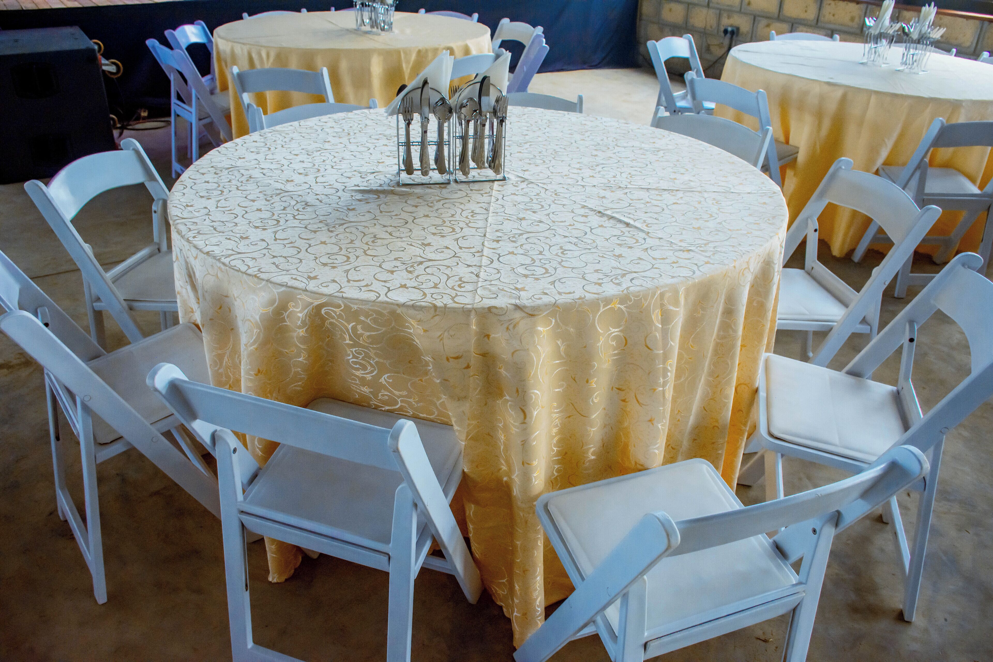 Des tables rondes entourées de chaises blanches, chaque table étant dressée avec des couverts et des serviettes.