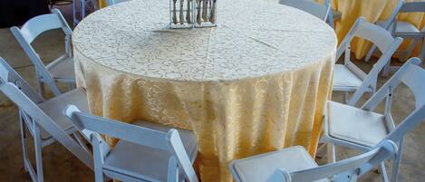 Des tables rondes entourées de chaises blanches, chaque table étant dressée avec des couverts et des serviettes.