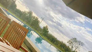 A poolside area with a wooden chair, a metal umbrella, and a view of the sky and trees. - Captain James Camp (Naivasha)